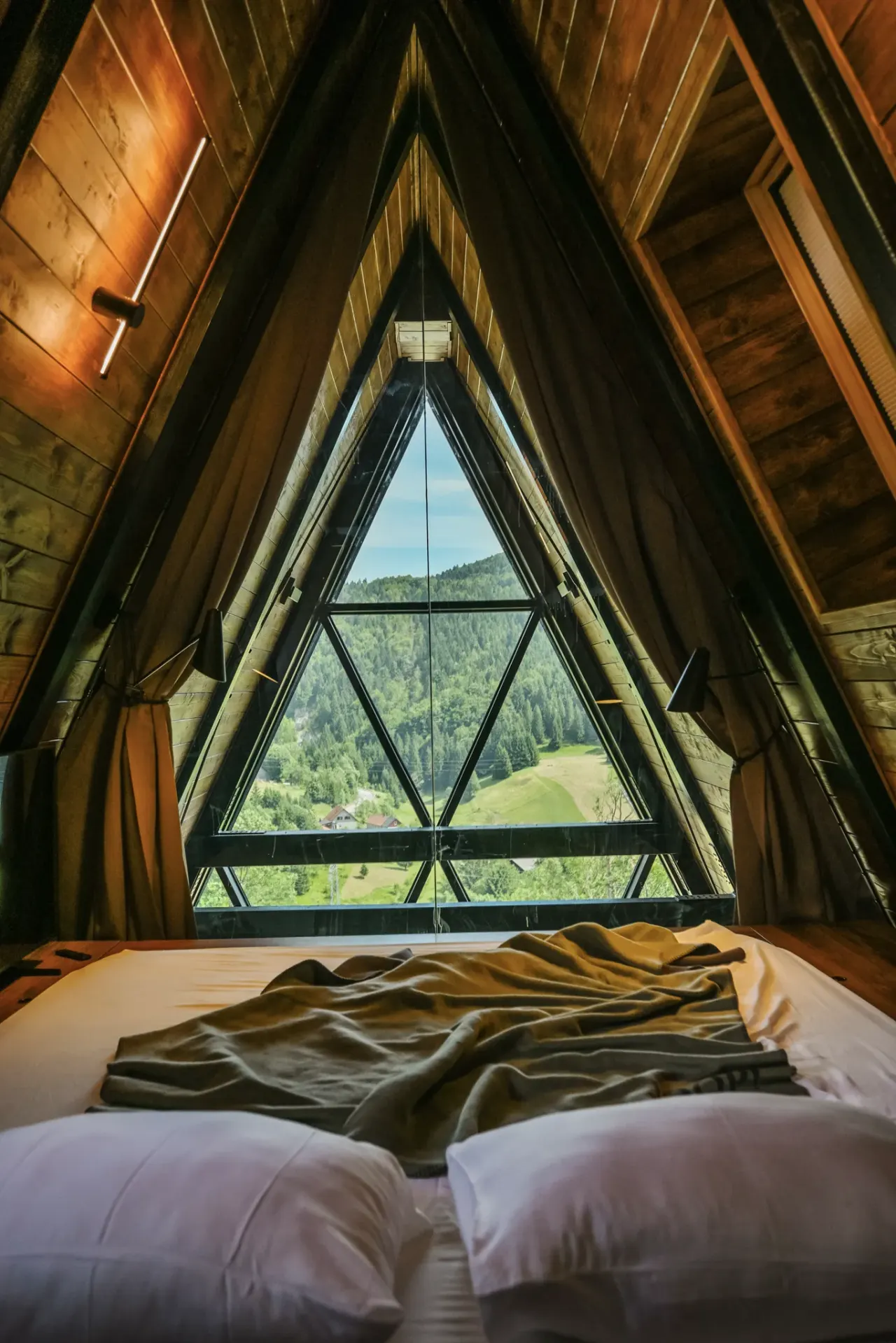 Upper peak bedroom framed by the triangular A-frame glass gable over the forest