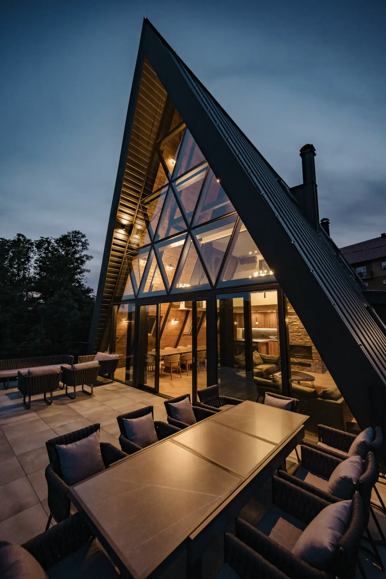 The black A-frame villa at dusk, its glass gable glowing above the terrace